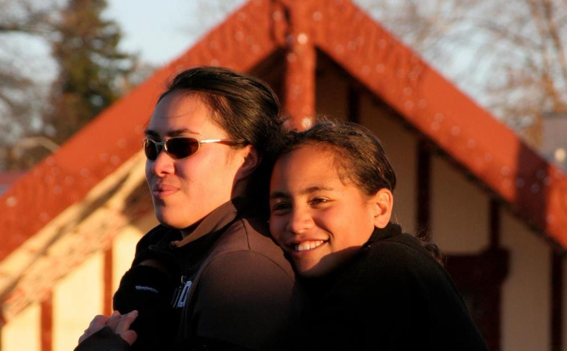 A mother and daughter hugging with a marae in the background